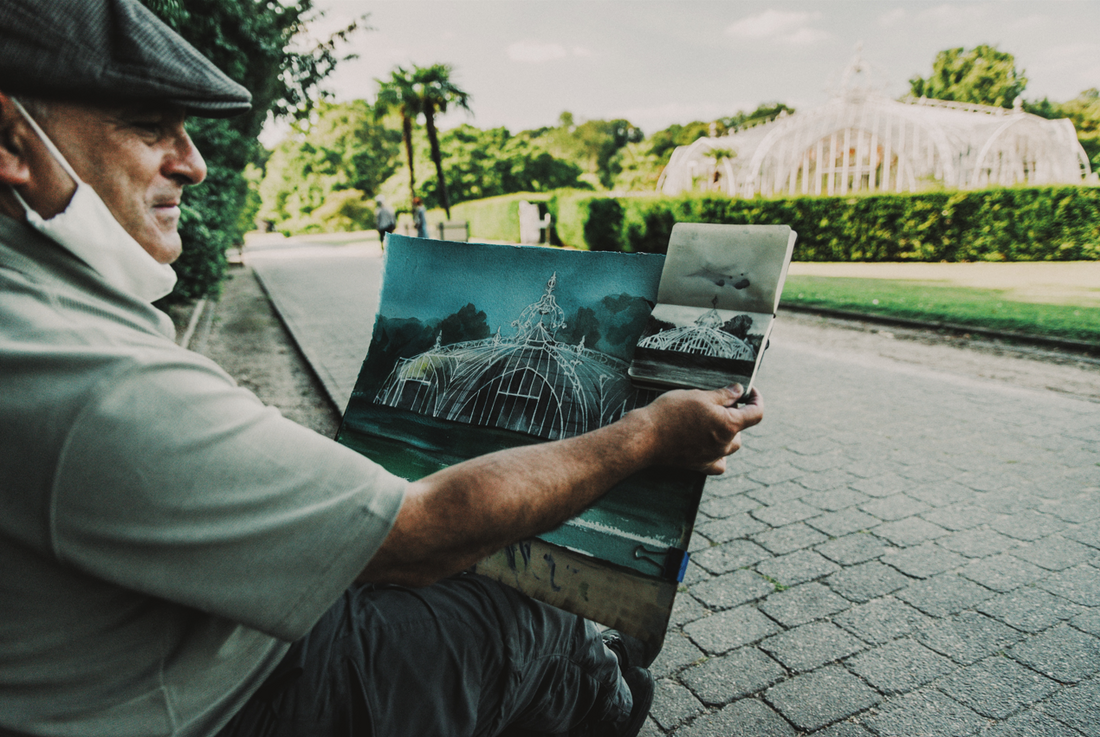 a watercolor artist compares his rough sketch to his final painting as he sits in front of his subject material: a geometric gated structure outside