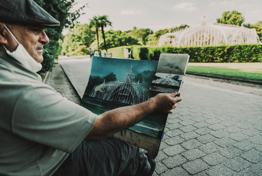 a watercolor artist compares his rough sketch to his final painting as he sits in front of his subject material: a geometric gated structure outside